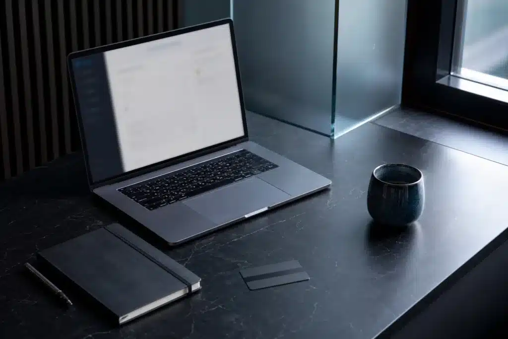 Dogecoin kaufen: Fragen vor dem Kauf 8 Laptop, leeres Notizbuch und umgedrehte Bankkarte auf einem Rechercheplatz am Fenster