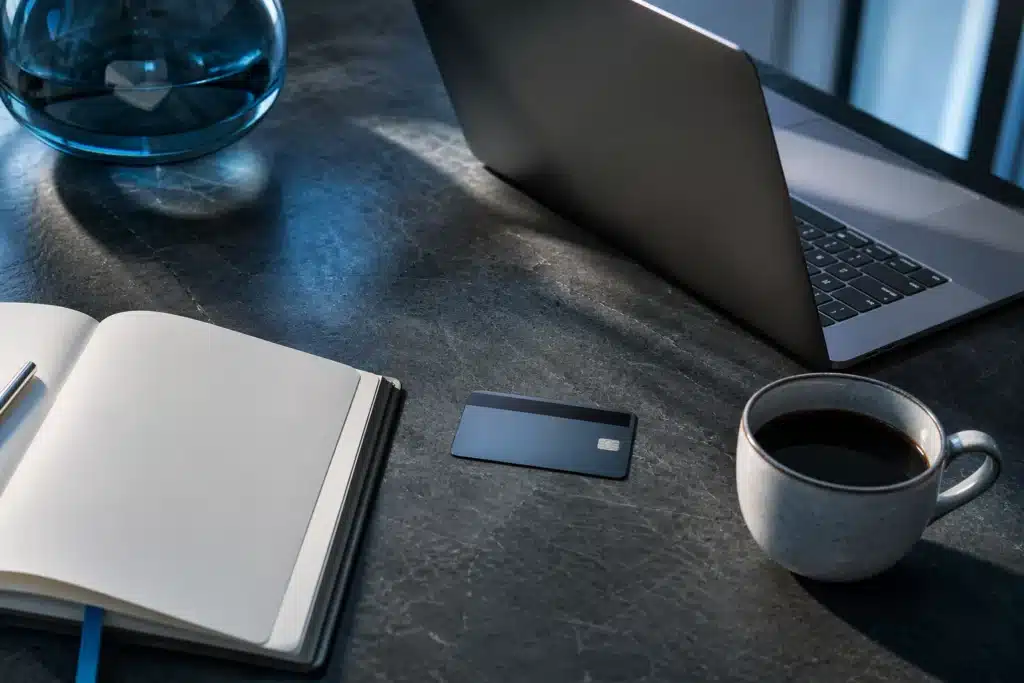 Laptop, face-down bank card and notebook arranged for reviewing purchase documentation